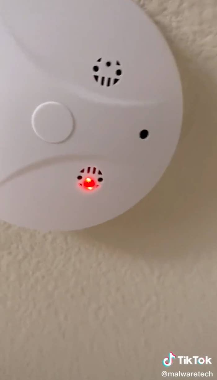 A closeup of a smoke alarm, which has a red light and a small empty hole