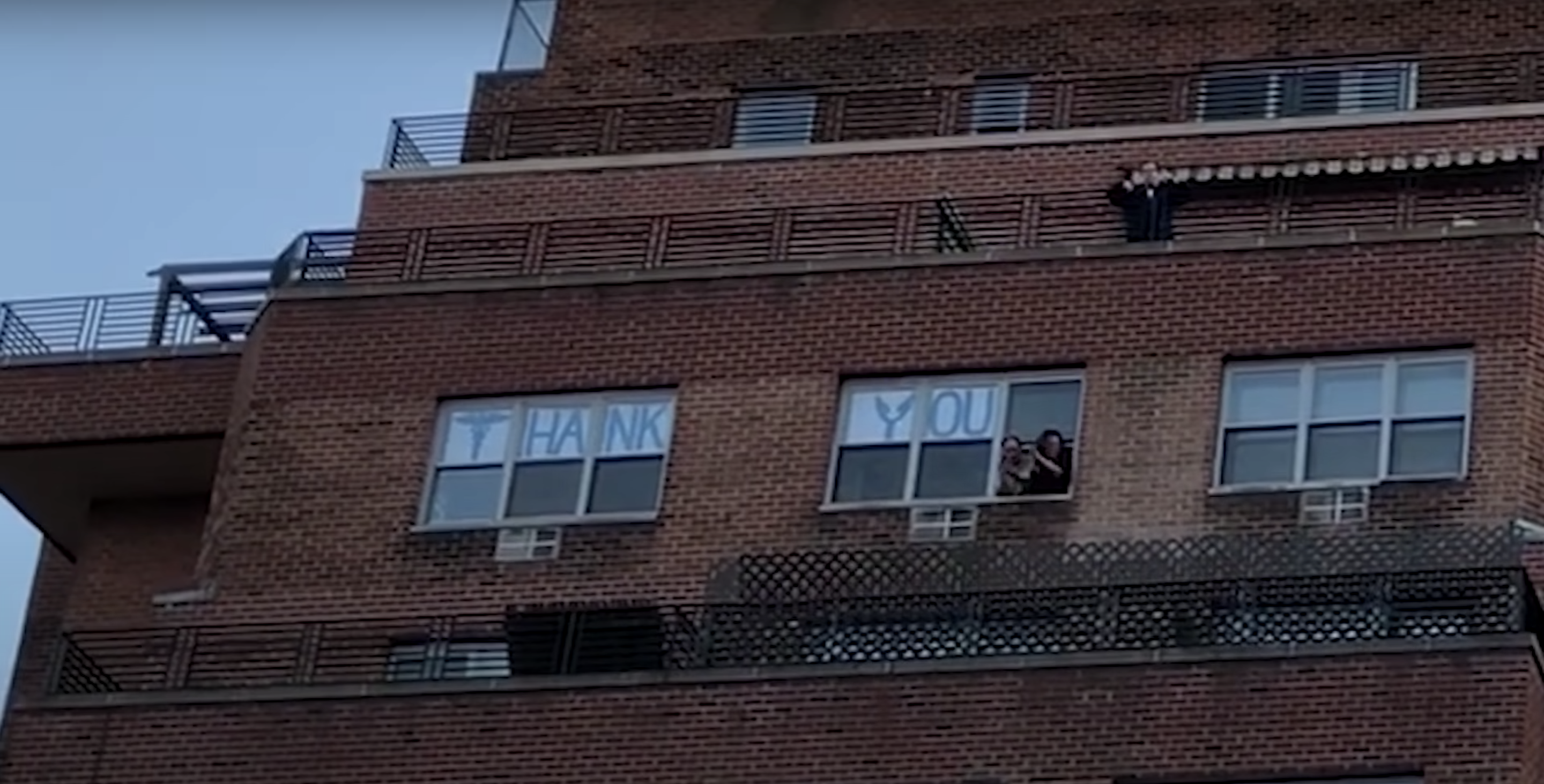 A &quot;Thank You Sign&quot; is shown through windows of a building as people look out the window and applaud