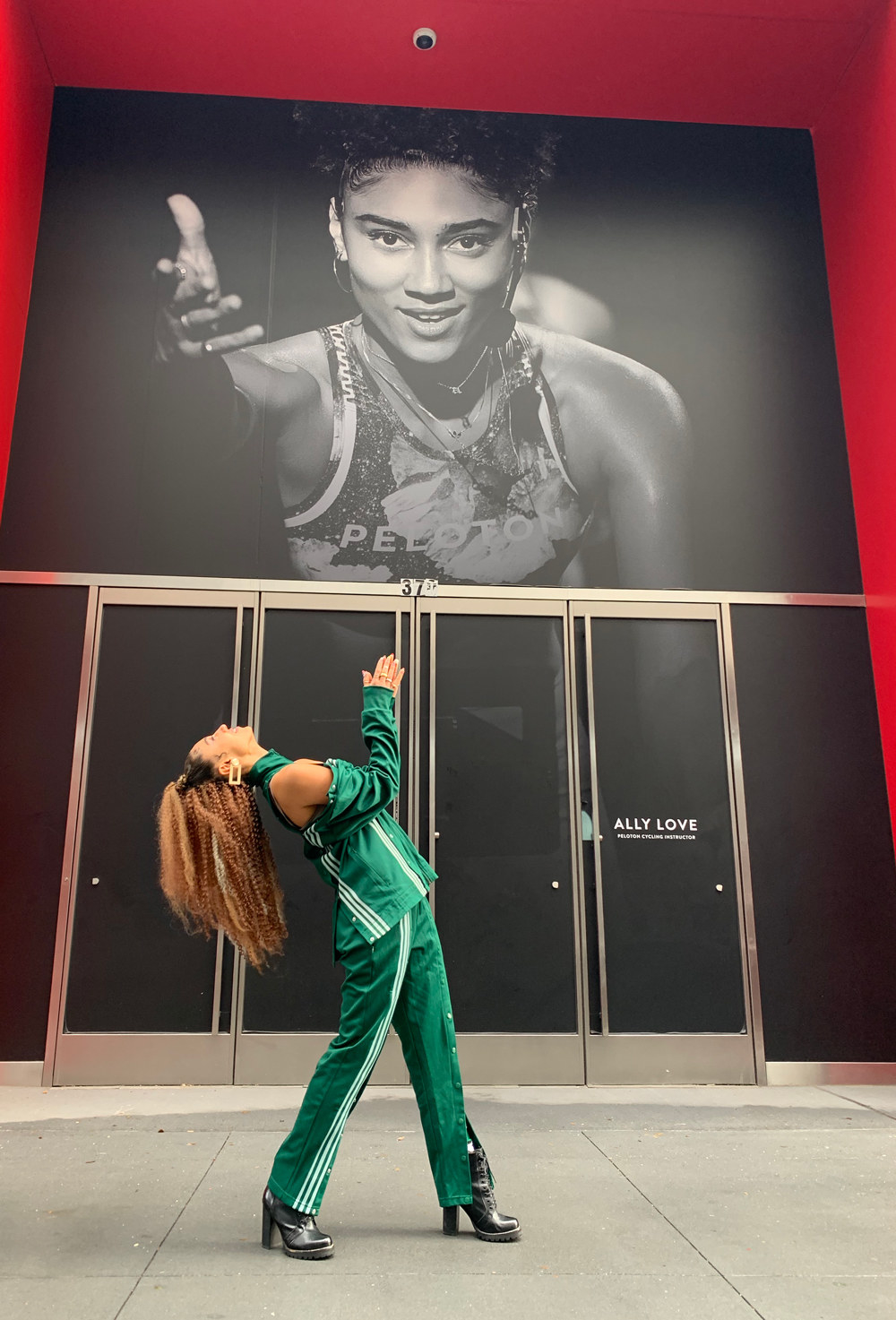 A smiling woman stands, leaning back beneath a poster of herself, and claps