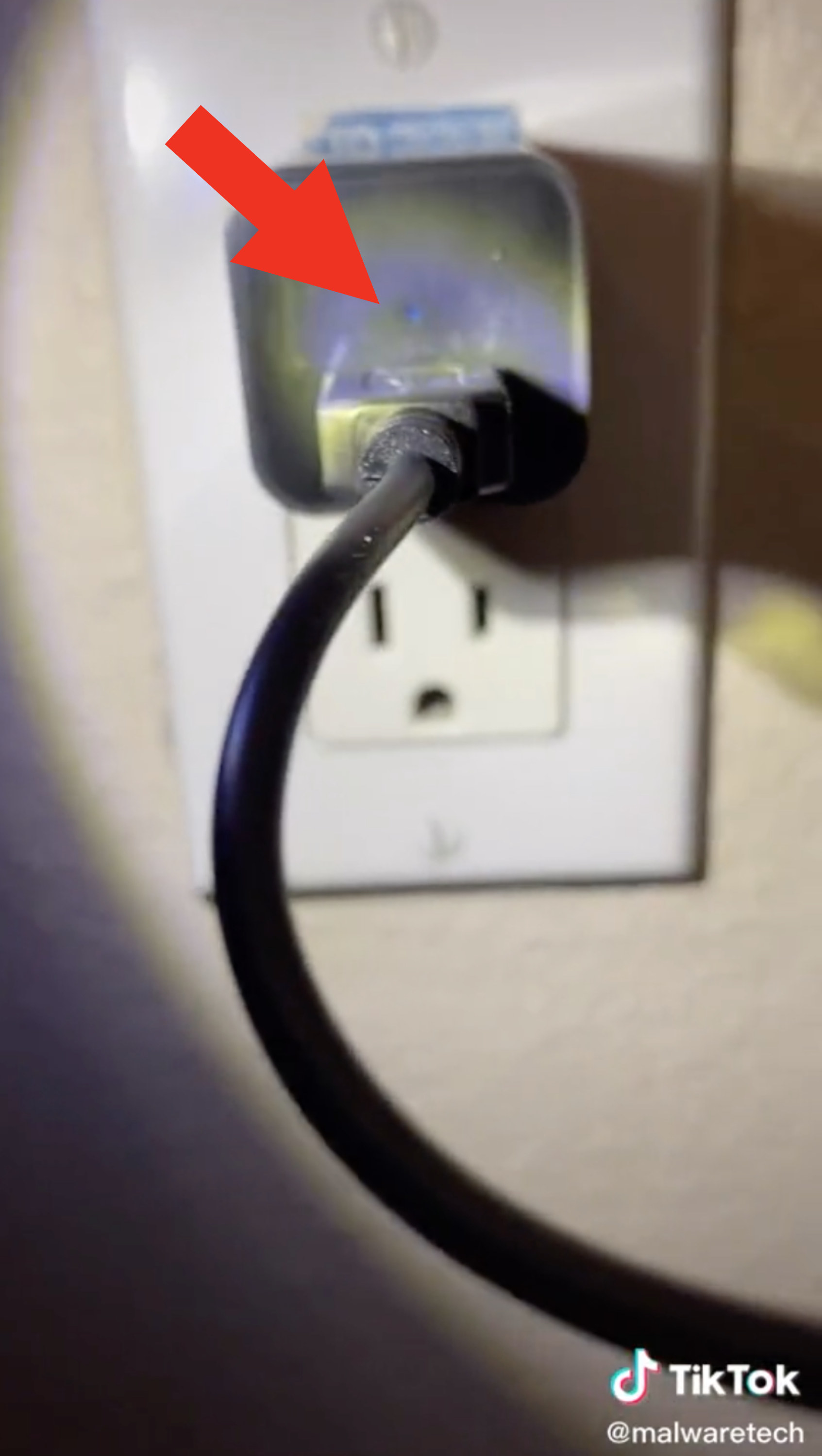 A closeup of a charger cord plugged into a wall, and you can see a tiny blue light above the cord
