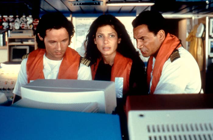 Sandra looks at a computer while wearing a life jacket with two men beside her