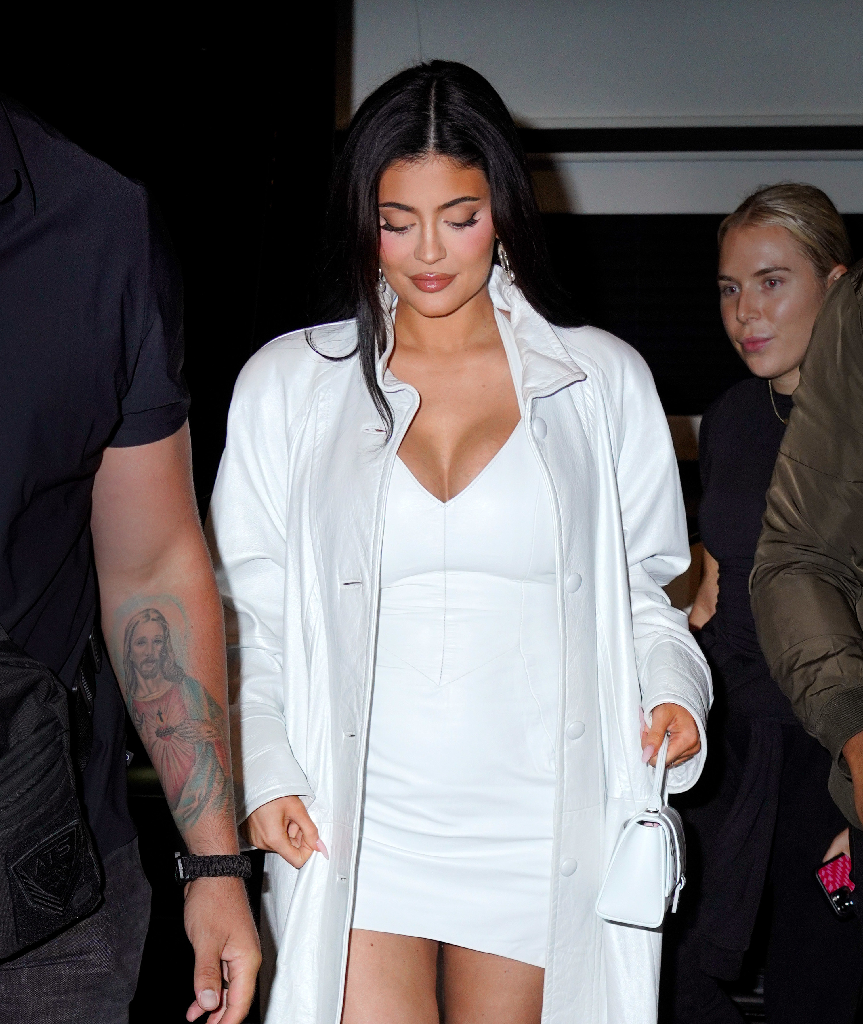 Kylie walks out of a building while wearing a big coat