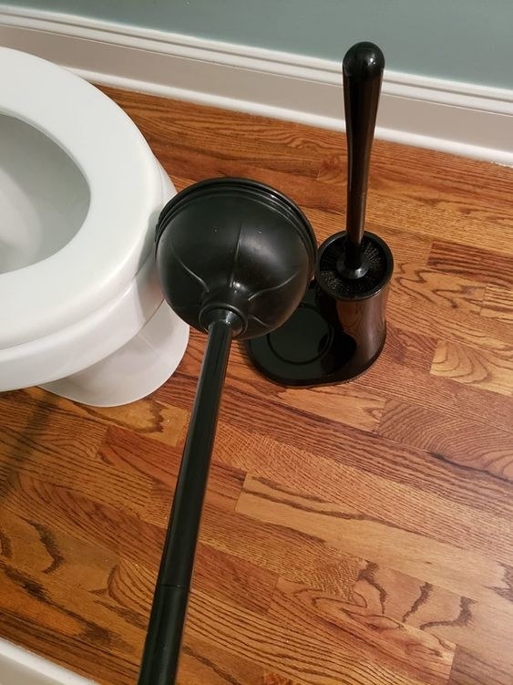 Reviewer&#x27;s black plunger next to storage caddy and toilet bowl