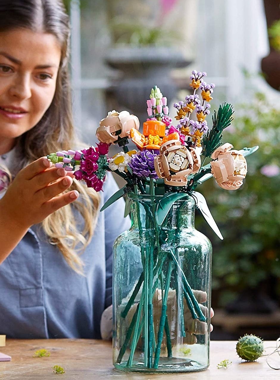A person touching the floral arrangement while it sits in a vase.