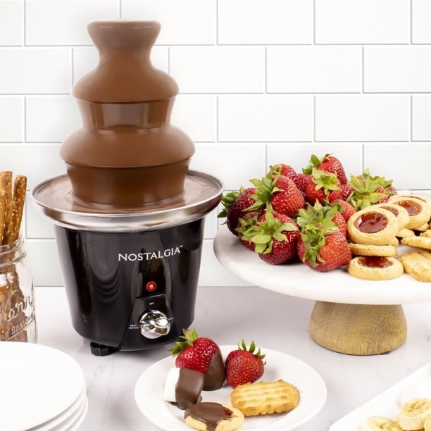 the chocolate fountain with fruit and other biscuits next to it