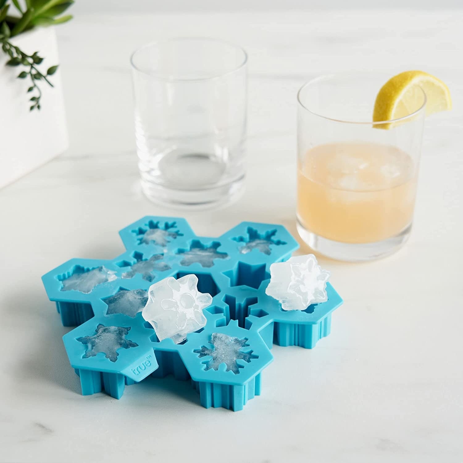 The ice cube tray in front of two glasses on a marble counter