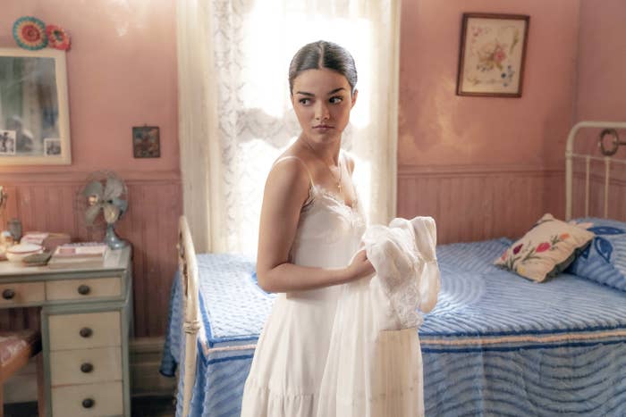 Zegler holds a white dress as she stands by a beed in a scene from West Side Story