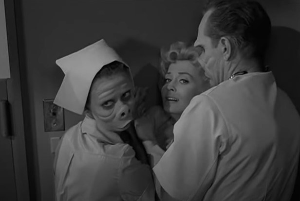 Two frightful looking hospital staff members wrangle a frightened female patient