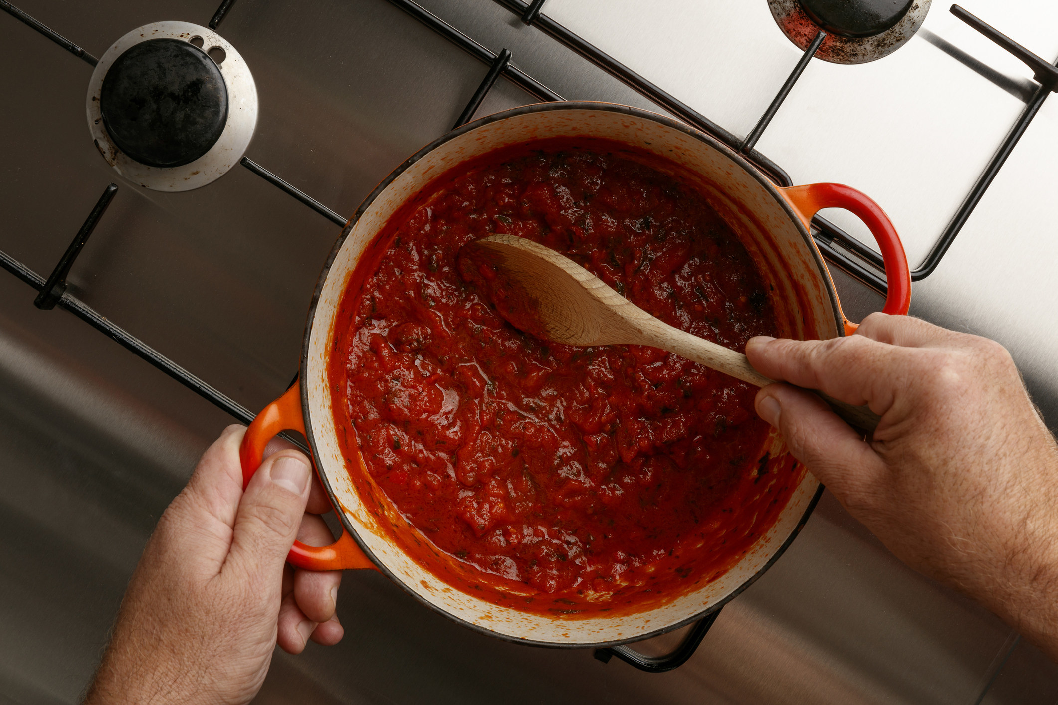 Cooking a tomato sauce on a stove-top with a wooden spoon