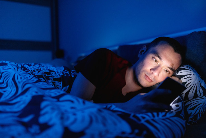 Person on their phone in bed while their partner sleeps