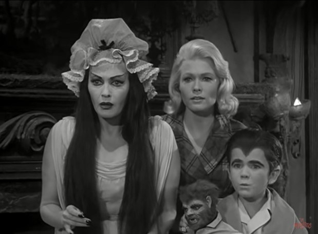 A female vampire and her werewolf son stand on either side of a young, blonde-haired woman