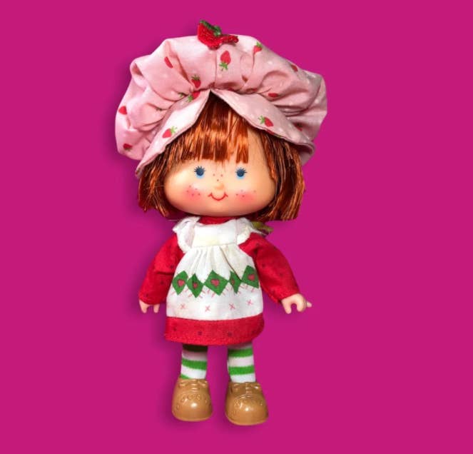 Old-school Strawberry Shortcake doll against a hot pink background
