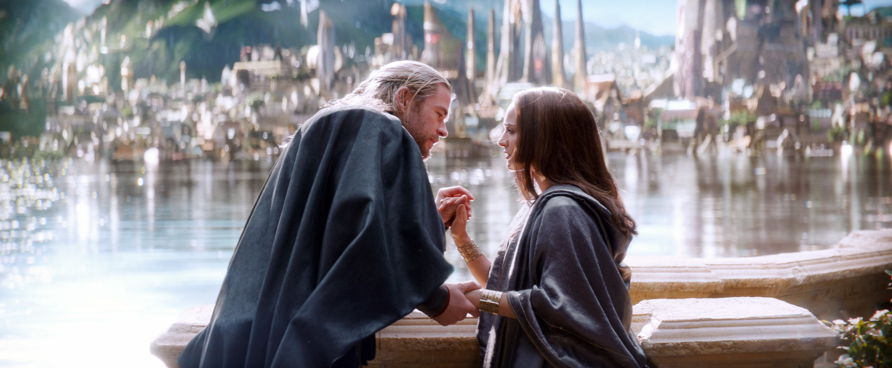 as they stand before a glittering lake on Asgard, Thor and Jane hold hands and gaze lovingly into each other&#x27;s eyes