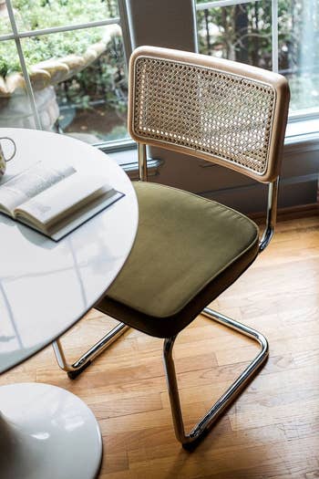 Modern chair with a woven backrest next to a round table with an open book on it, indoor setting