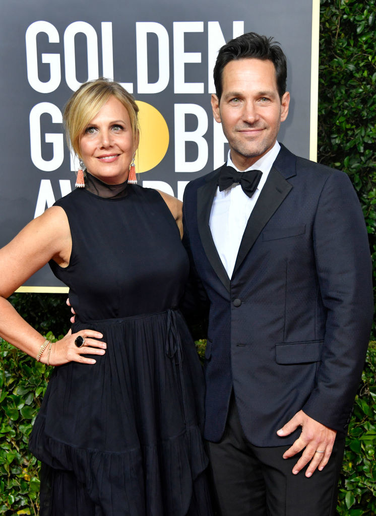 standing close together on the red carpet, Julie wears a sleeveless dress with a tulle turtleneck and tiered skirt, and Paul wears a traditional tux in a matching color