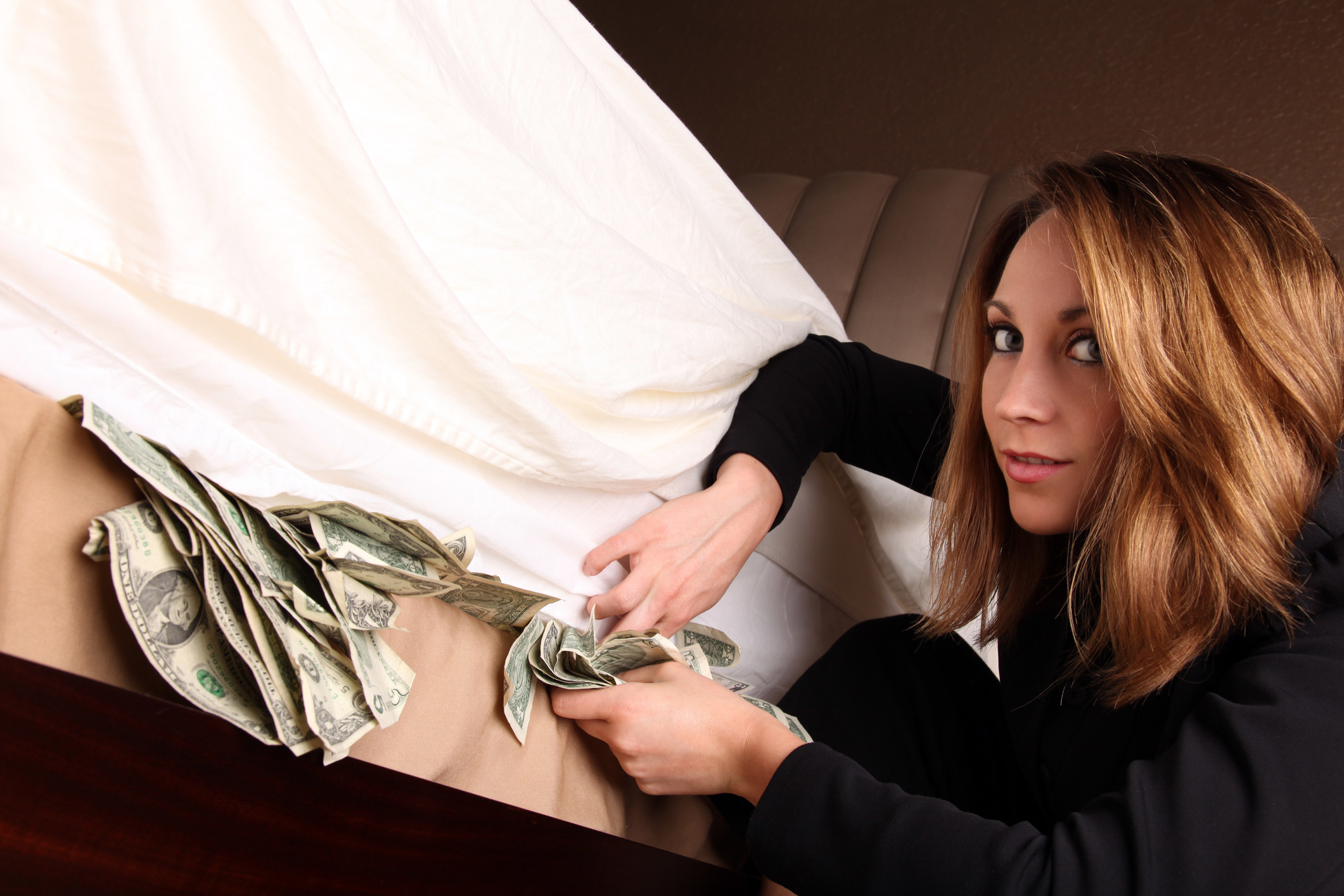 Woman stuffing cash under a mattress