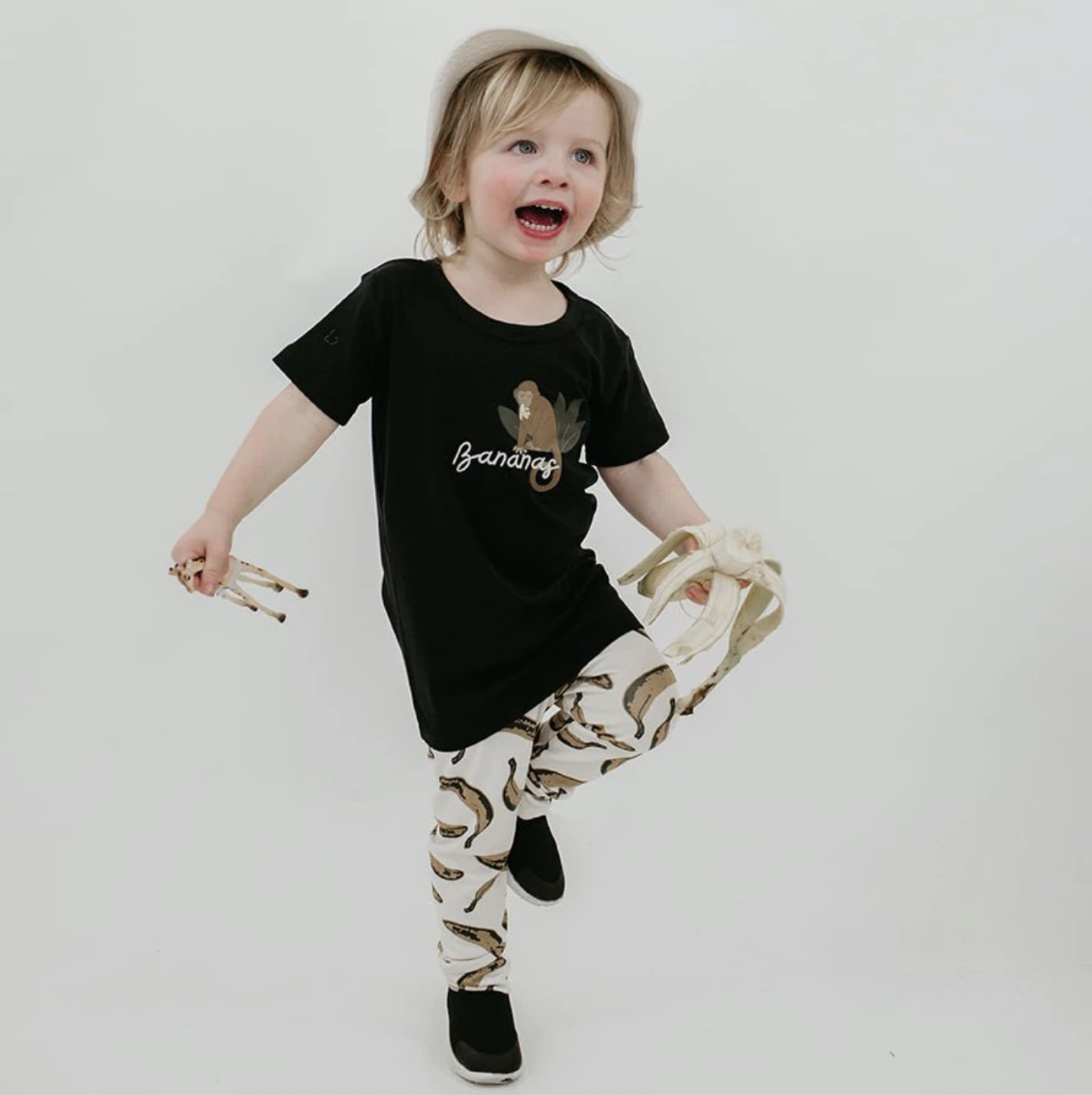 A kid wearing the banana leggings with a monkey shirt while holding a giraffe toy and a banana
