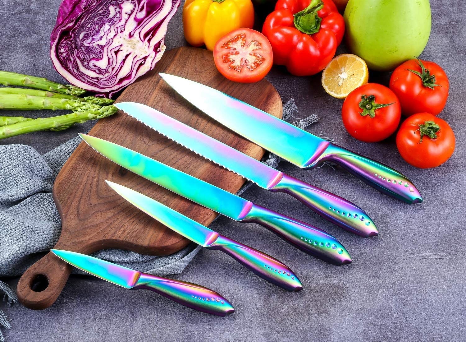 a set of rainbow kitchen knives next to fresh fruits and veggies