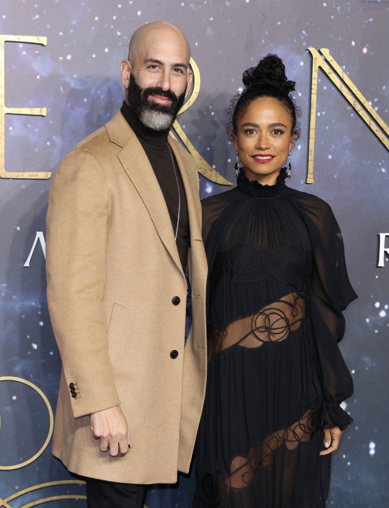 standing together on the red carpet, Douglas wears a long coat, and Lauren wears a long-sleeved dress with a turtleneck, tulle pleats, and stripes of sheer mesh