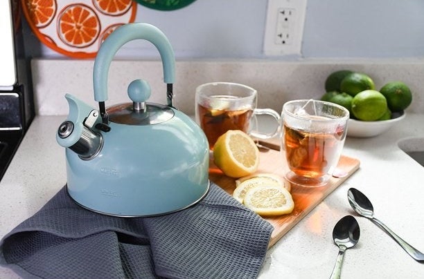 the mint green teapot on a kitchen counter next to a lemon and two cups of tea