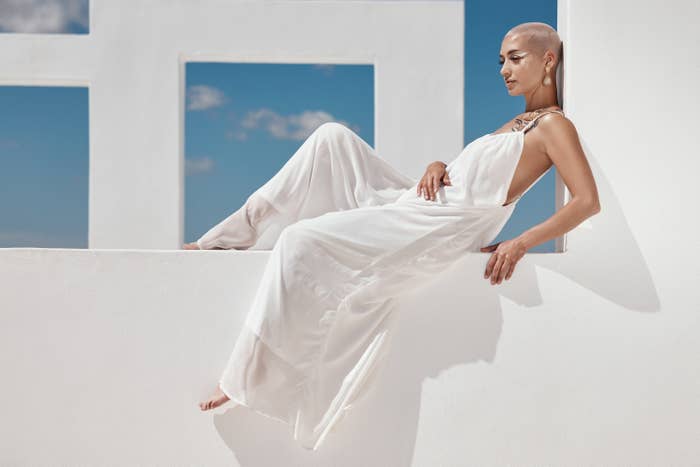 A woman in a buzz cut and white jump suit sitting on a white wall window