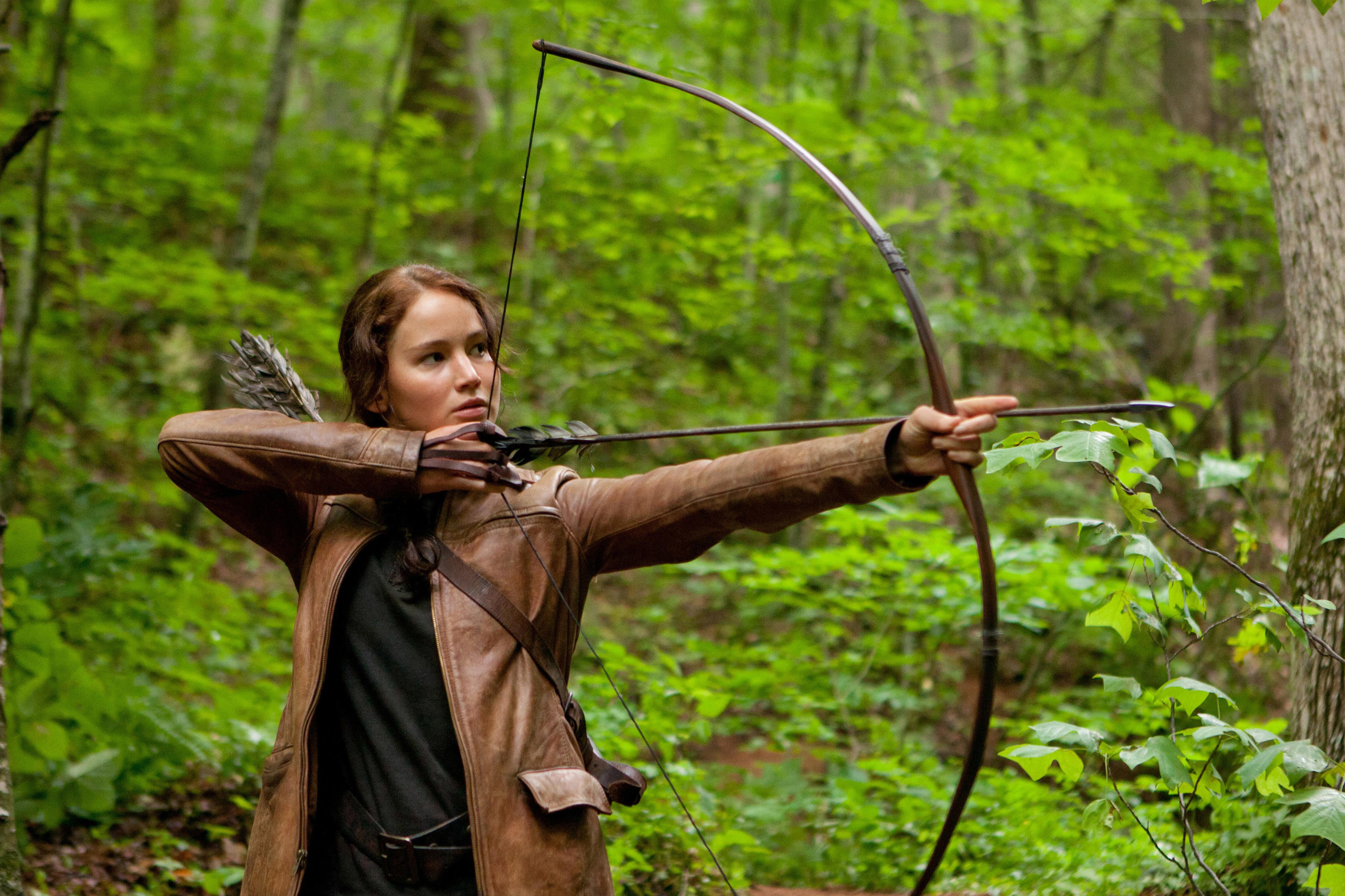 Katniss using a bow and arrow amid trees