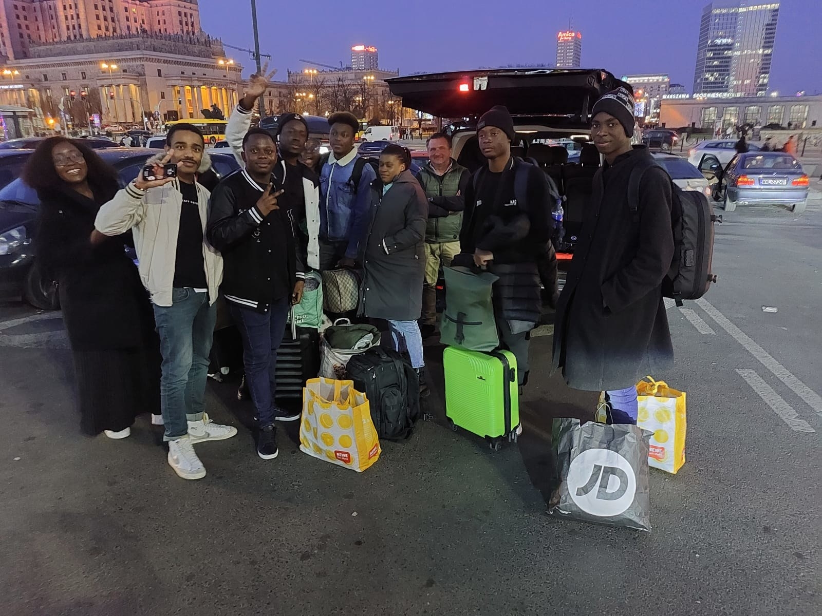 A group of people smile and make peace signs for the camera outside in a city