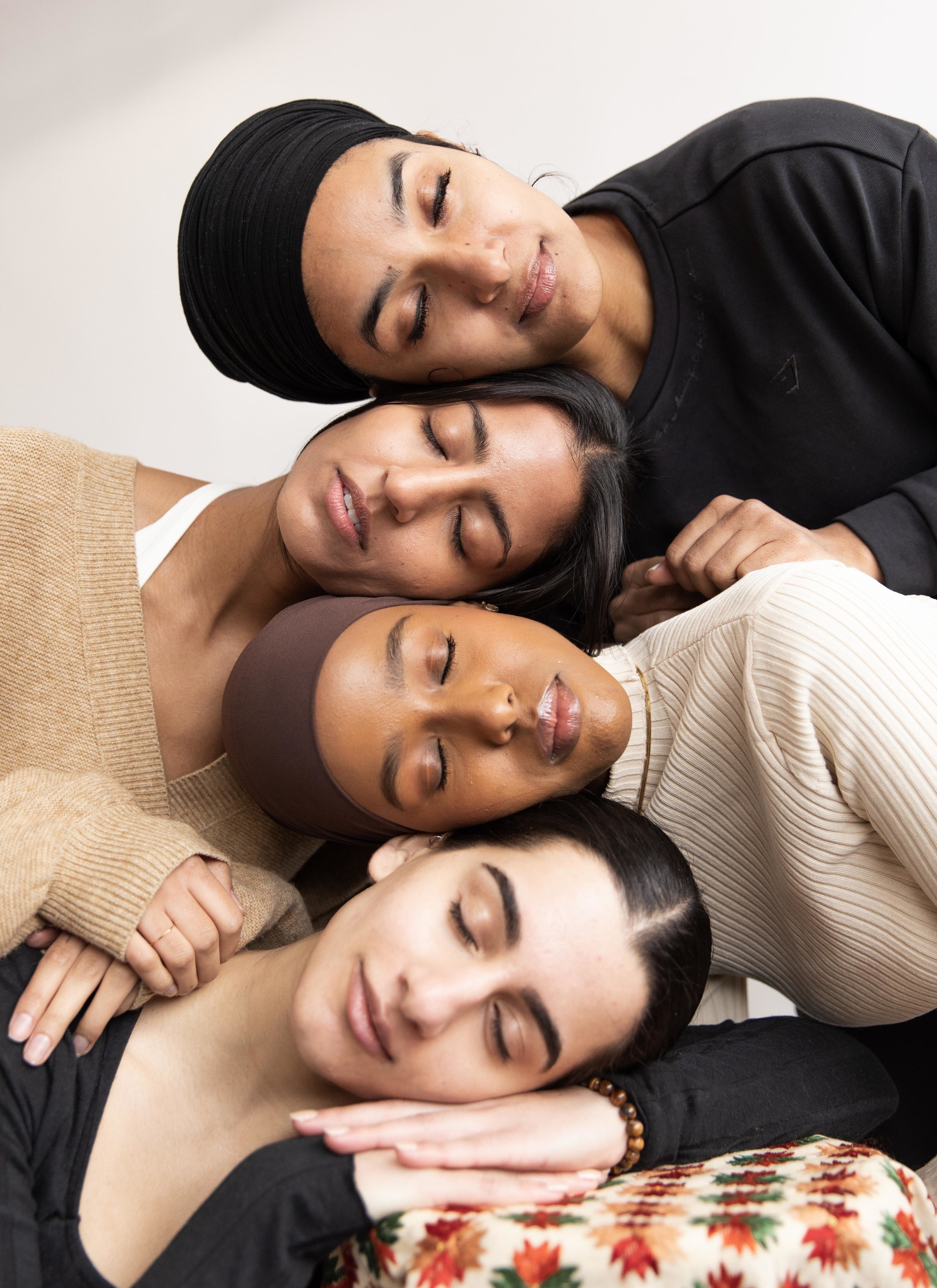 four people of different skin types and tones laying their heads on top of one another
