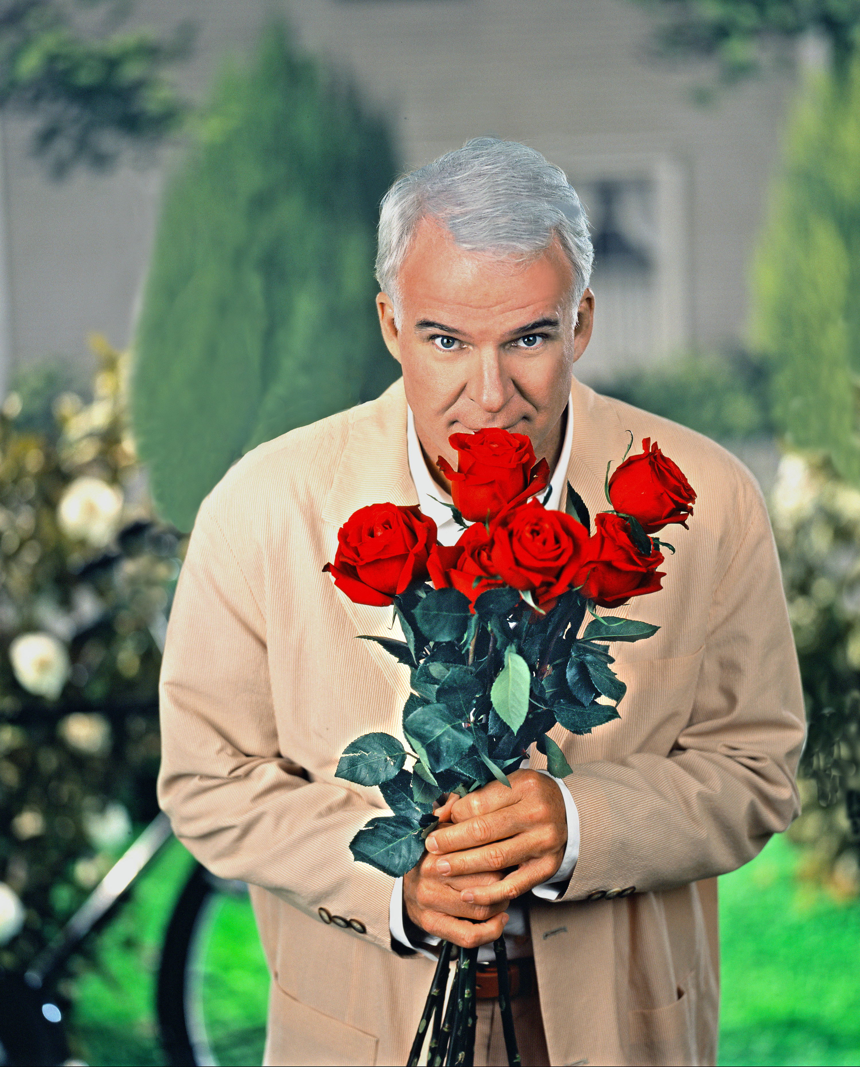 Steve Martin holds a bouquet of roses in a garden