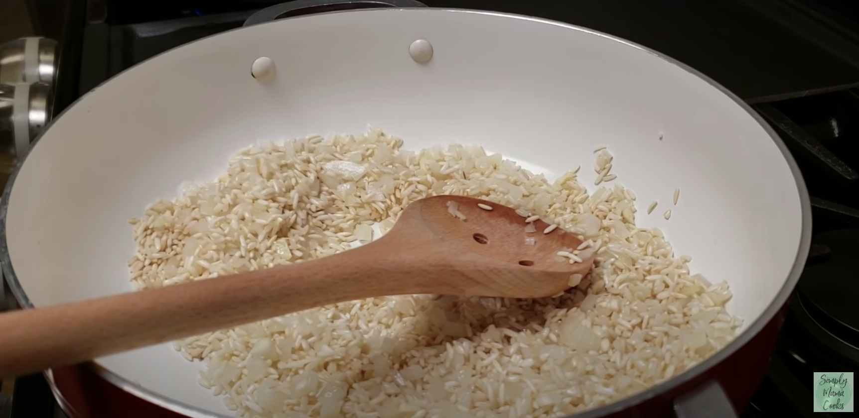 Dry rice in a pan on a stove with a wooden spoon