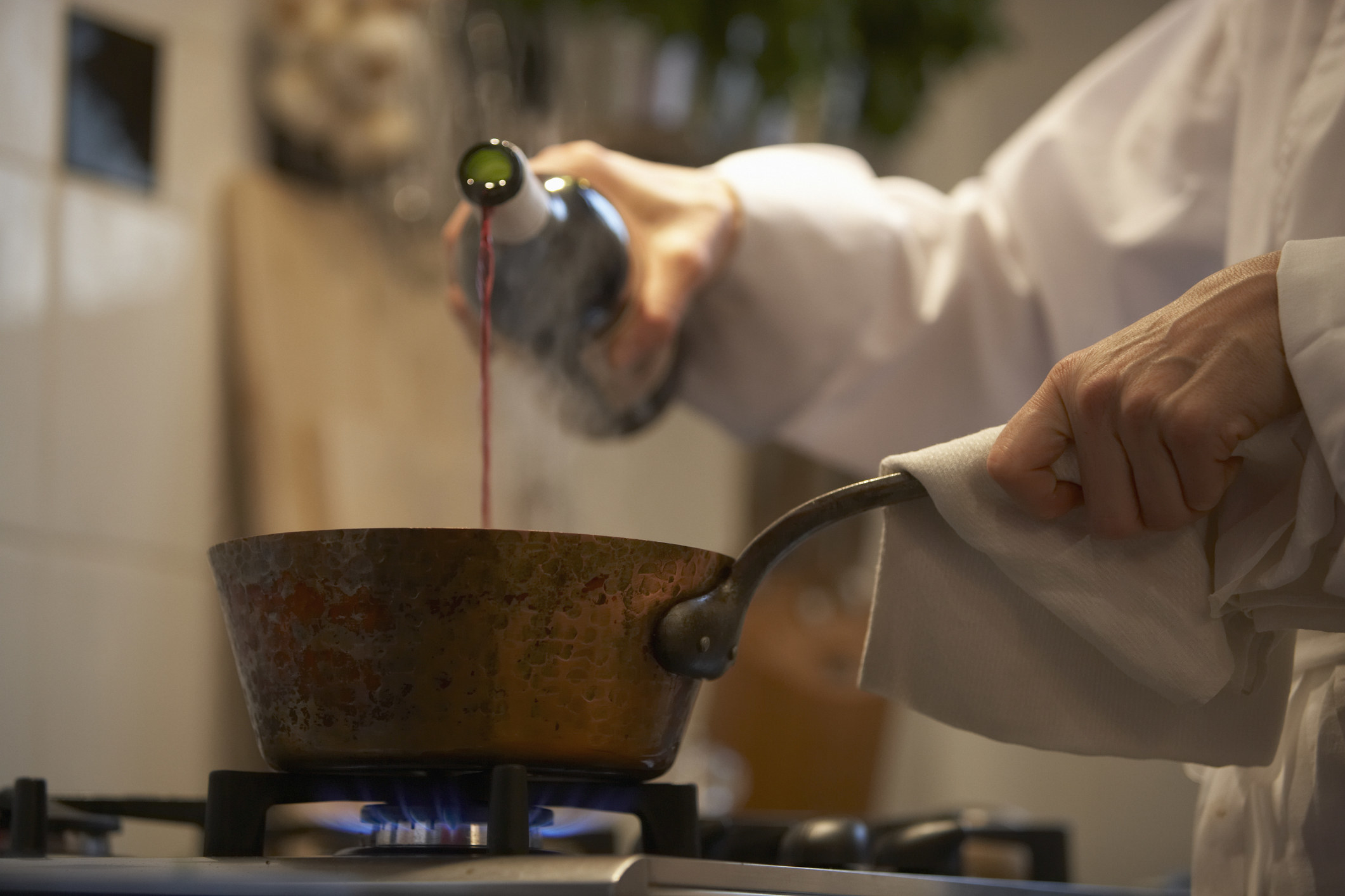 A chef pouring wine into a pot on a lit stove