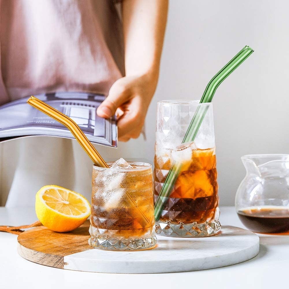 a green reusable straw and an orange reusable straw both in drink glasses