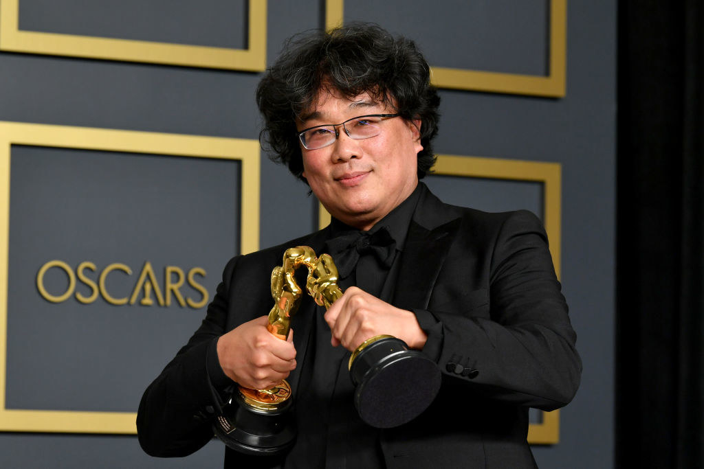 Bong Joon-ho holds two Oscar statues in his hands and makes them kiss each other