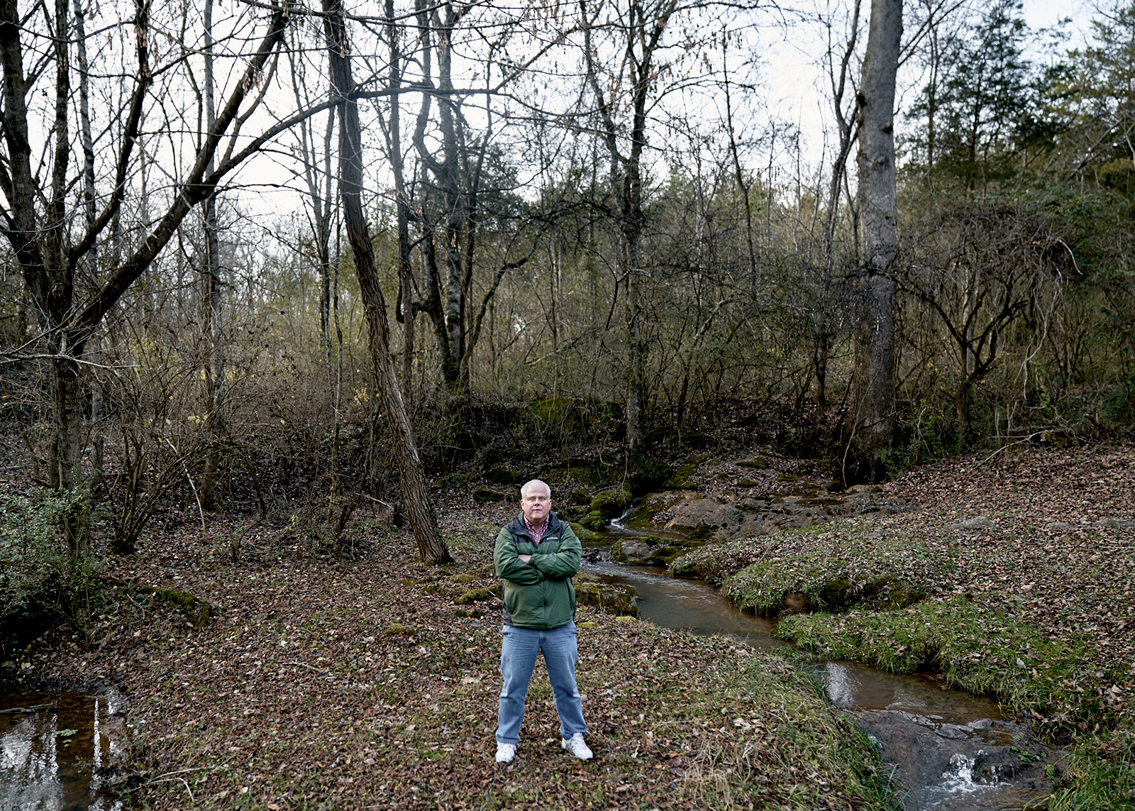 A man standing in the woods with his arms crossed