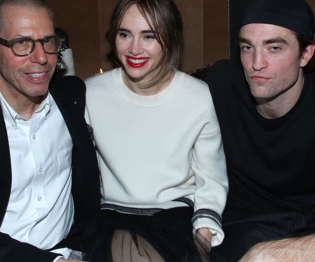 sitting together at a table, Rob puts his arm around Suki