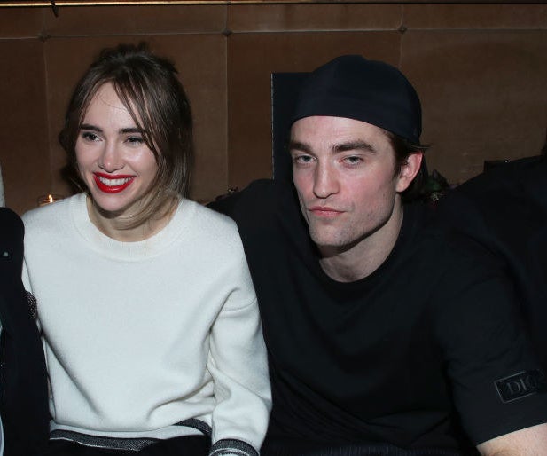 sitting together at a table, Rob puts his arm around Suki