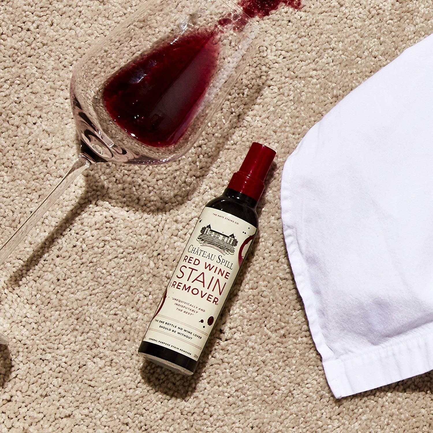 A bottle of the wine stain remover next to a spilt glass of red wine