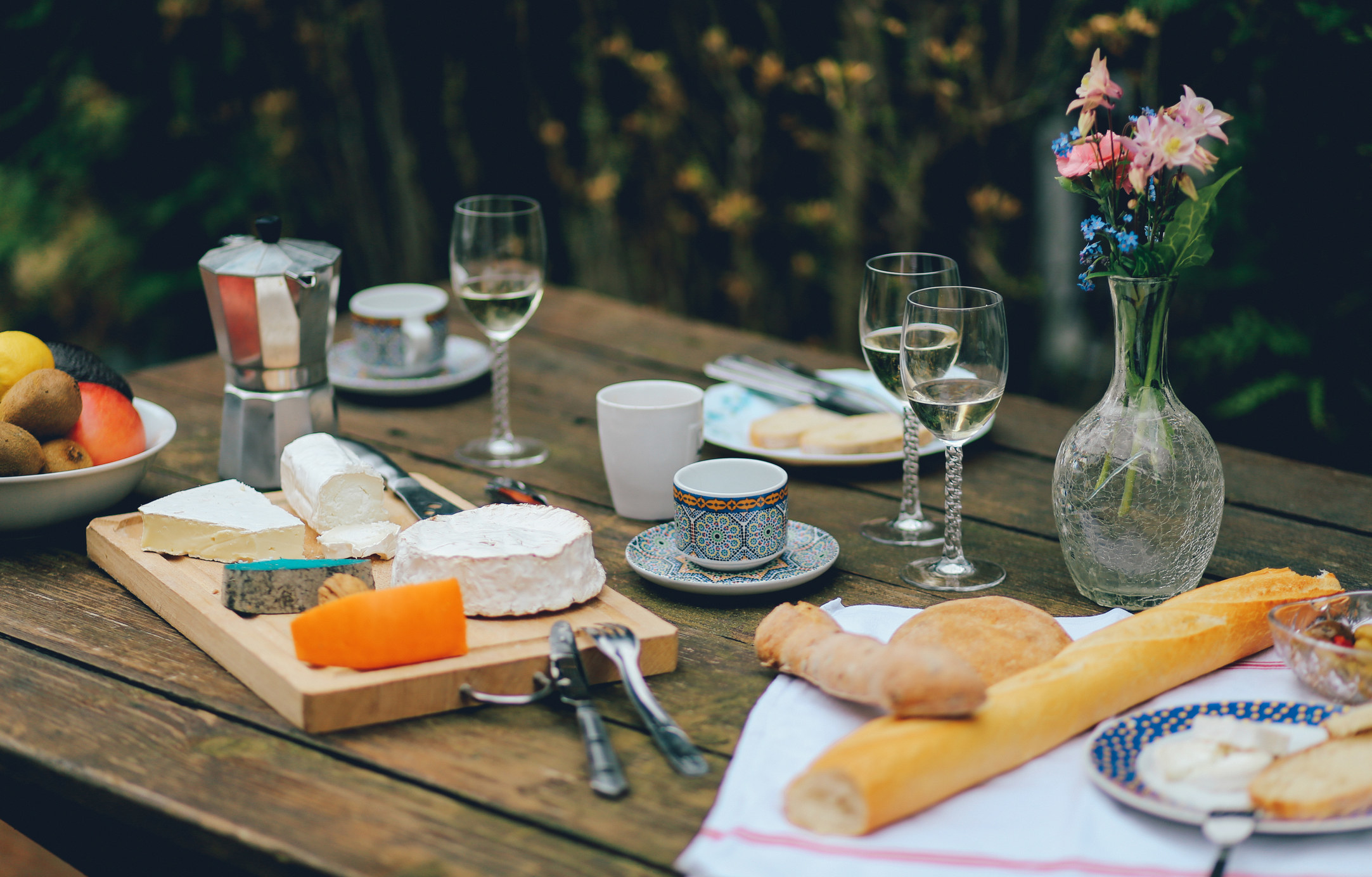 a spread of cheese, bread and wine on a picnic table