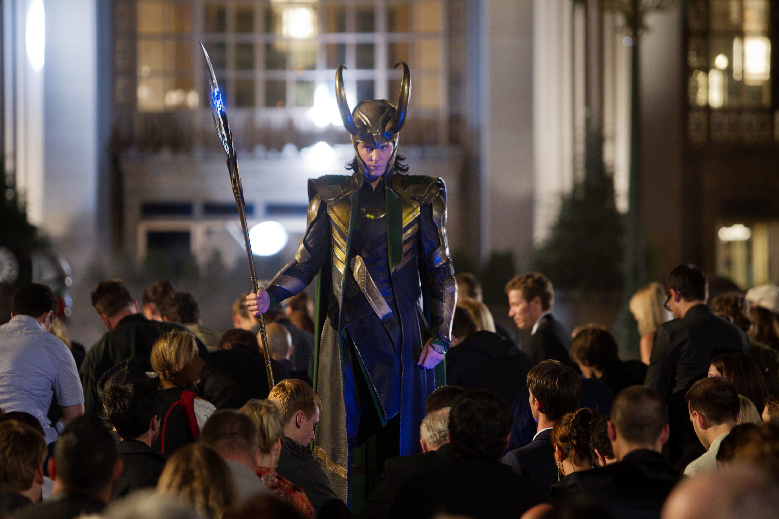 Loki holding his scepter and walking amongst kneeling people