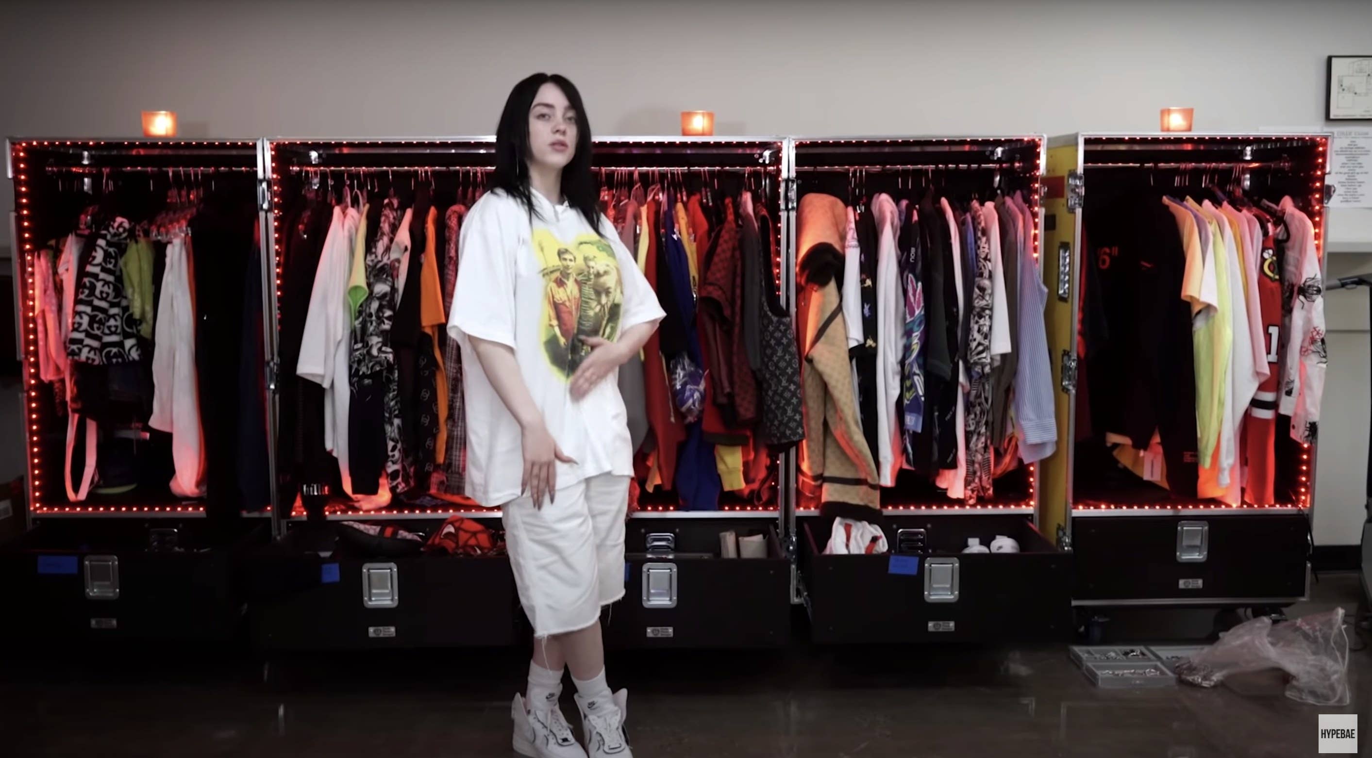 Billie stands in front of several road cases filled with clothing that is hung up