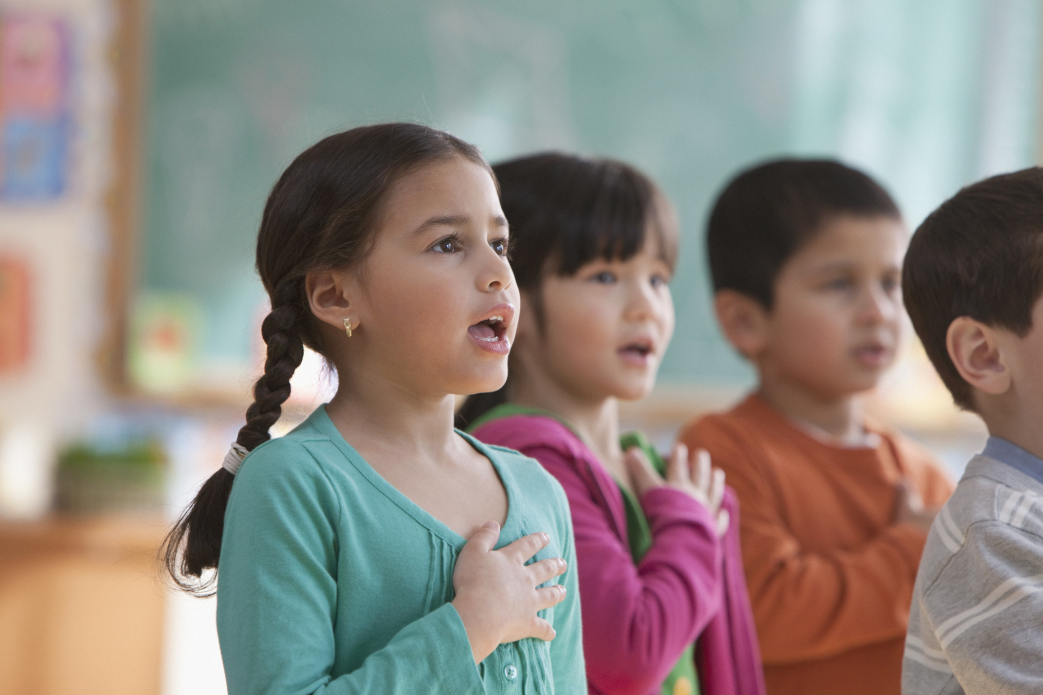 A group of children in a classroom reciting the pledge with their hands over their hearts