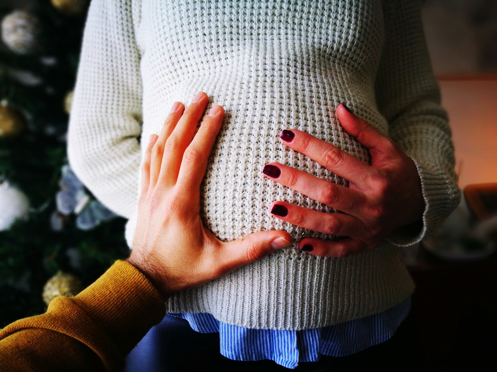A hand cupping the belly of a pregnant person wearing a sweater