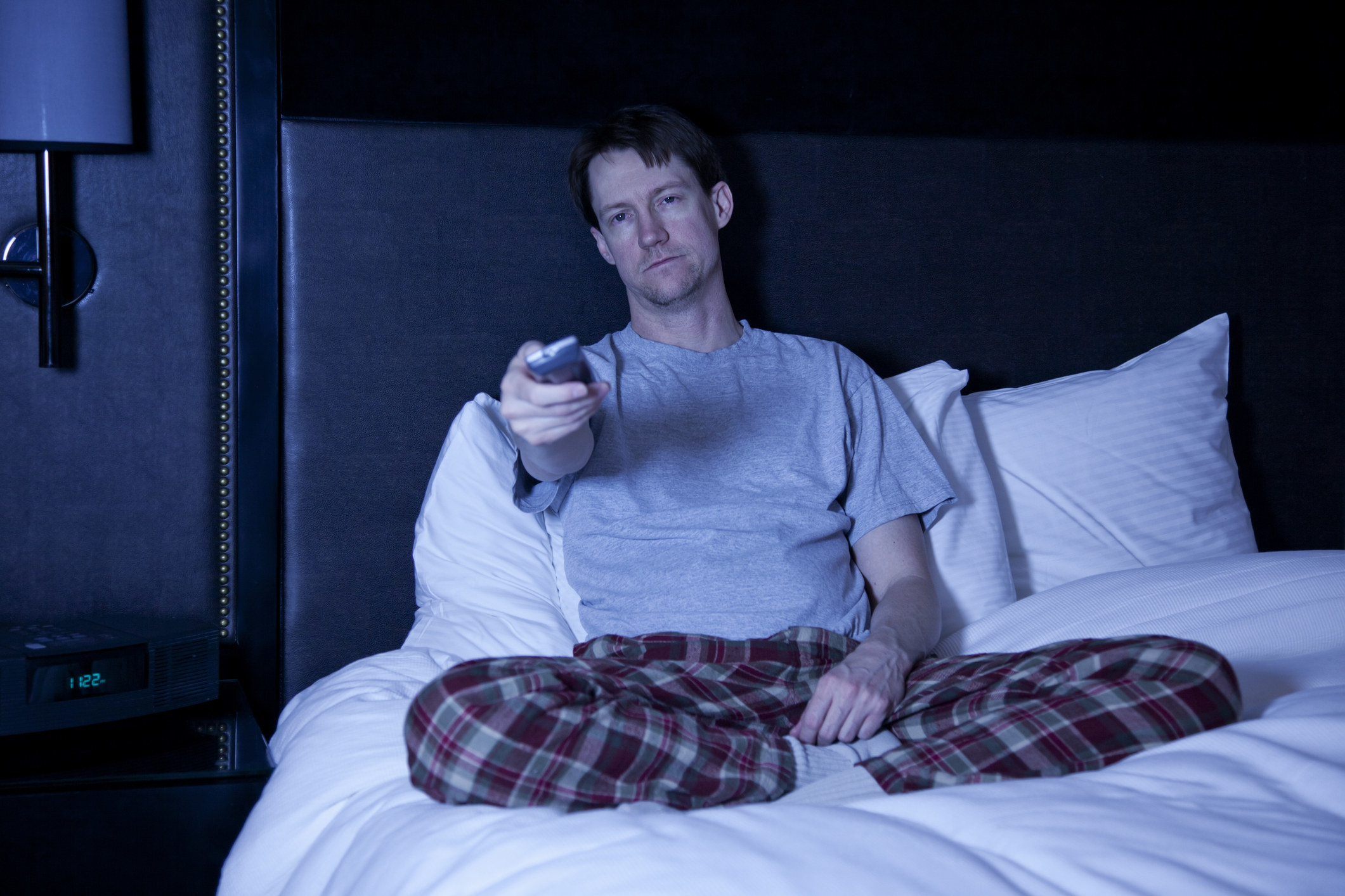 A man sitting in bed clicking the remote control