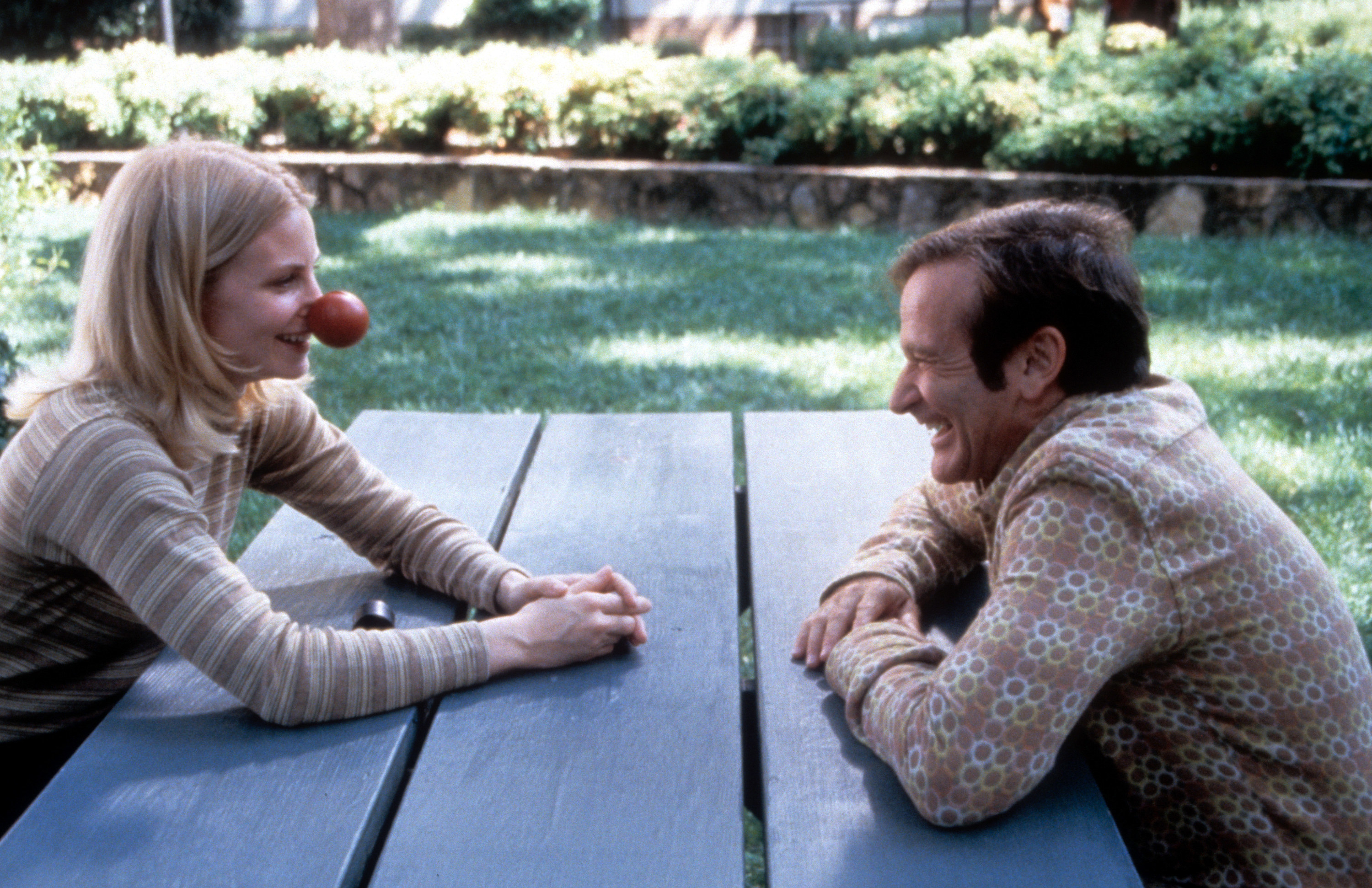Robin Williams and Monica Potter sit cross from each other at a picnic table in a scene from &quot;Patch Adams&quot;