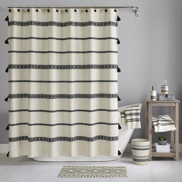 a cream colored shower curtain with black stripes and black tassels