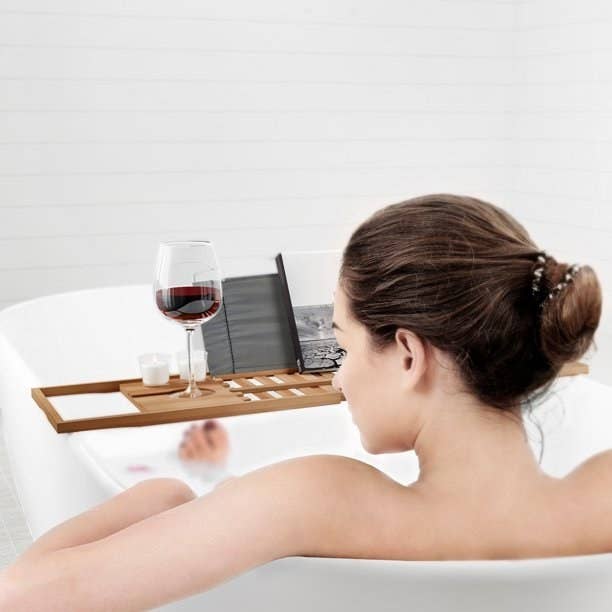 Model sitting in tub with wine and book on a wood bath tray