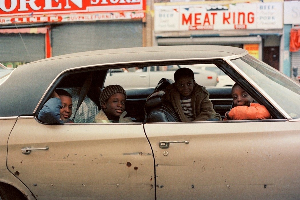 Smiling children sitting in a car with the windows down gaze at the camera