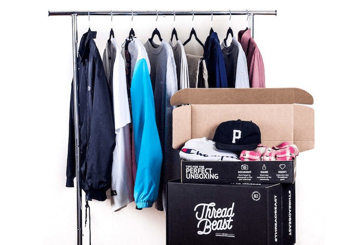 Assorted clothes hanging on a rack and a ThreadBeast box with clothes and a hat inside