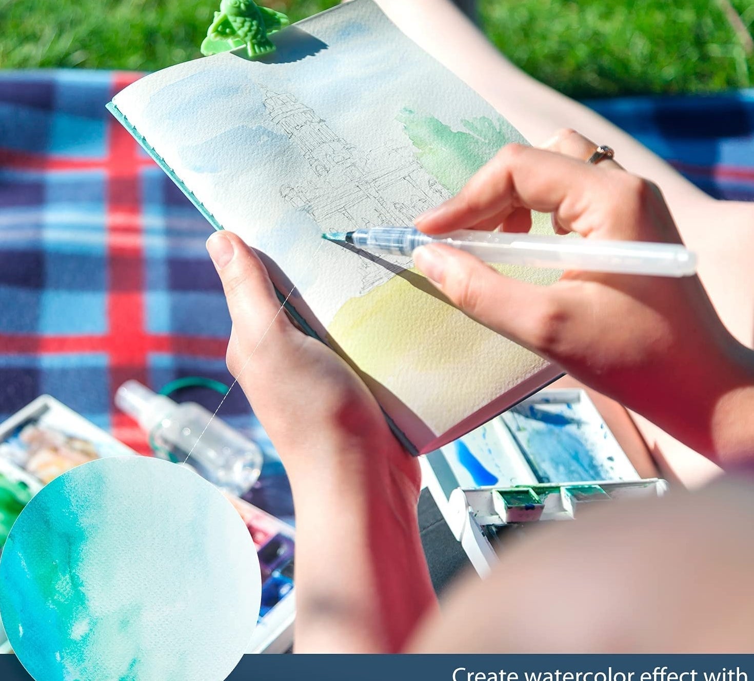 Someone using a watercolour brush pen on a sketch while outdoors on a flannel blanket