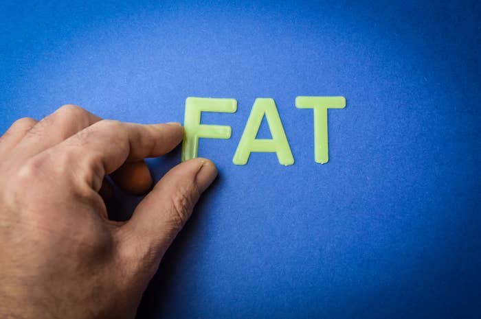 Human fingers remove the word Fat written with plastic letters on blue paper background